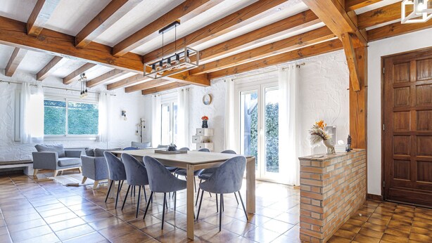 Une cuisine spacieuse avec un plafond en bois, un coin repas avec des chaises et une table, et une cheminée en briques.