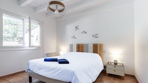 Une chambre à coucher comprenant un lit, une table de chevet, une lampe fixée au mur et une fenêtre.
