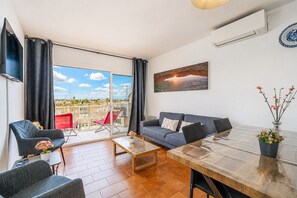 En moderne stue med sofa, stole, sofabord og udsigt til en balkon med røde stole.