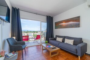 En stue med sofa, lænestol og sofabord, samt en balkon med røde stole og et billede på væggen.