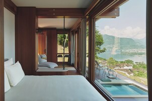 A bedroom with a large bed, a view of a lake, and a balcony with a pool.