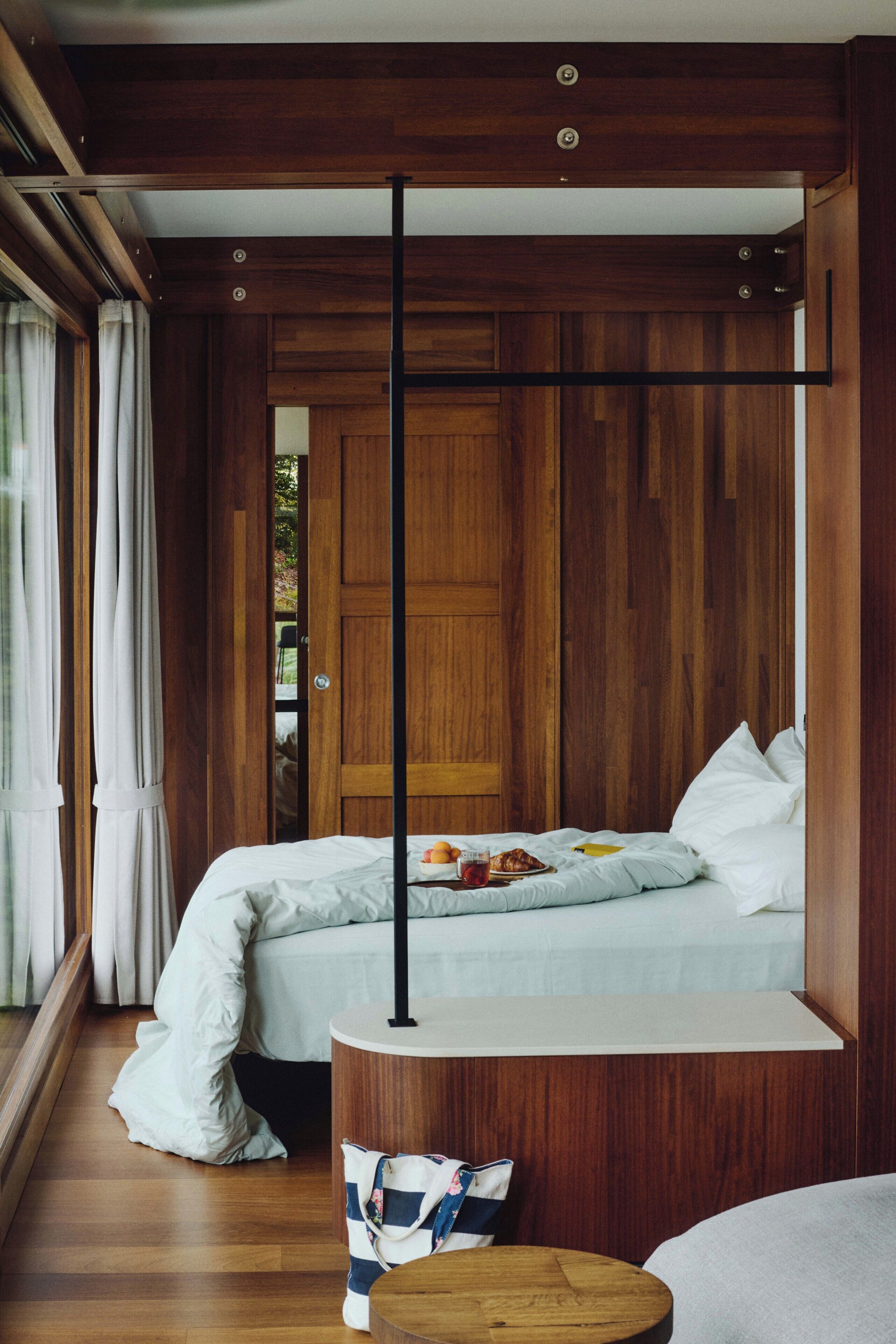Une chambre avec un plancher en bois, un lit avec une literie blanche, une table de chevet et une fenêtre avec des rideaux.