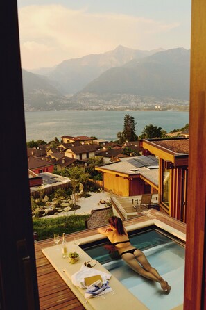A poolside view with a person relaxing, overlooking a mountainous landscape and a body of water. - Habitat Lago Maggiore (Gambarogno)