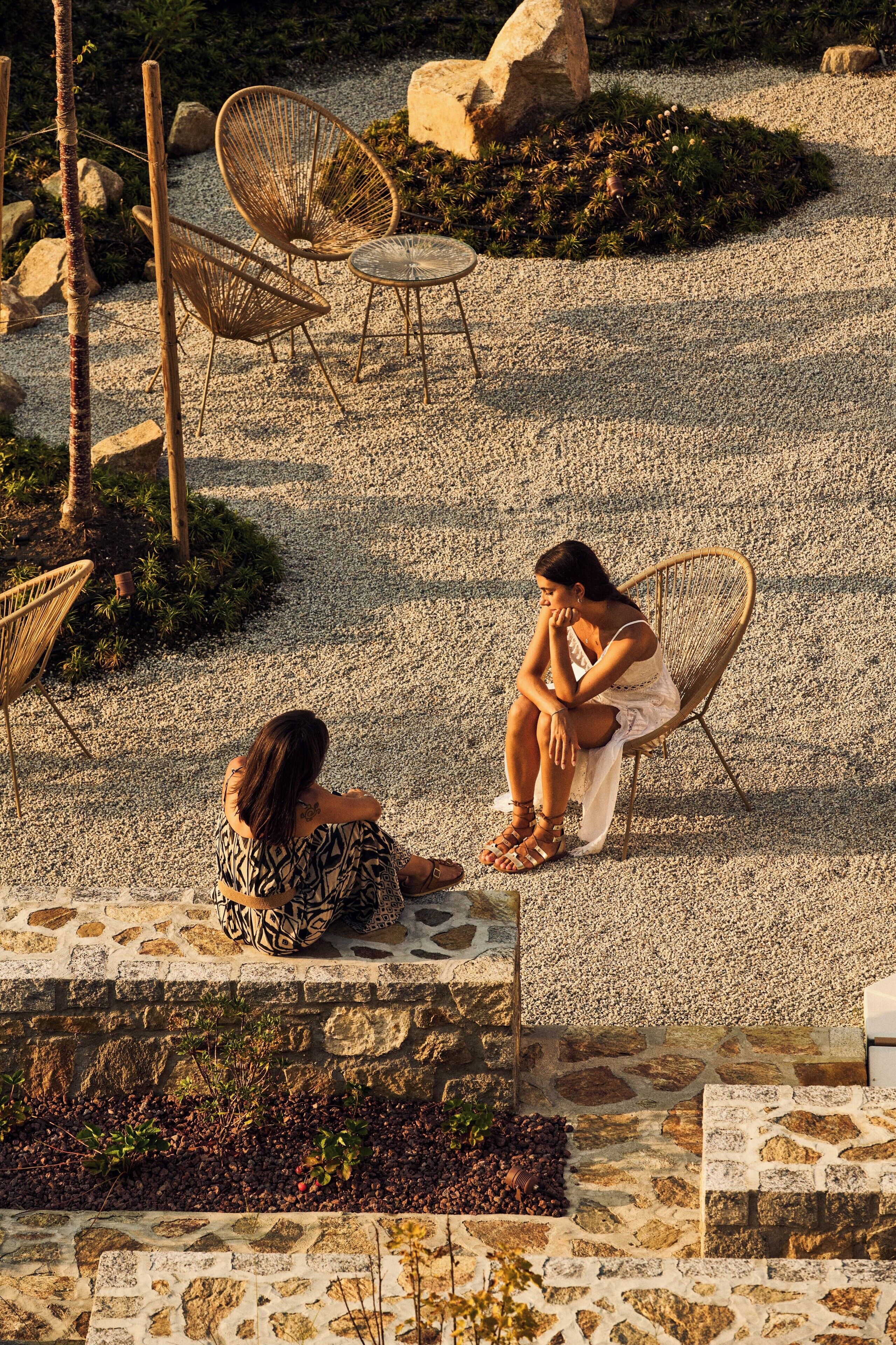 Eine Terrasse mit Korbstühlen und einem kleinen Tisch, umgeben von Kies und Pflanzen.