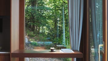 A room with a large window, two blue bar stools, a wooden table with a book and a cup, and a hanging pendant light.