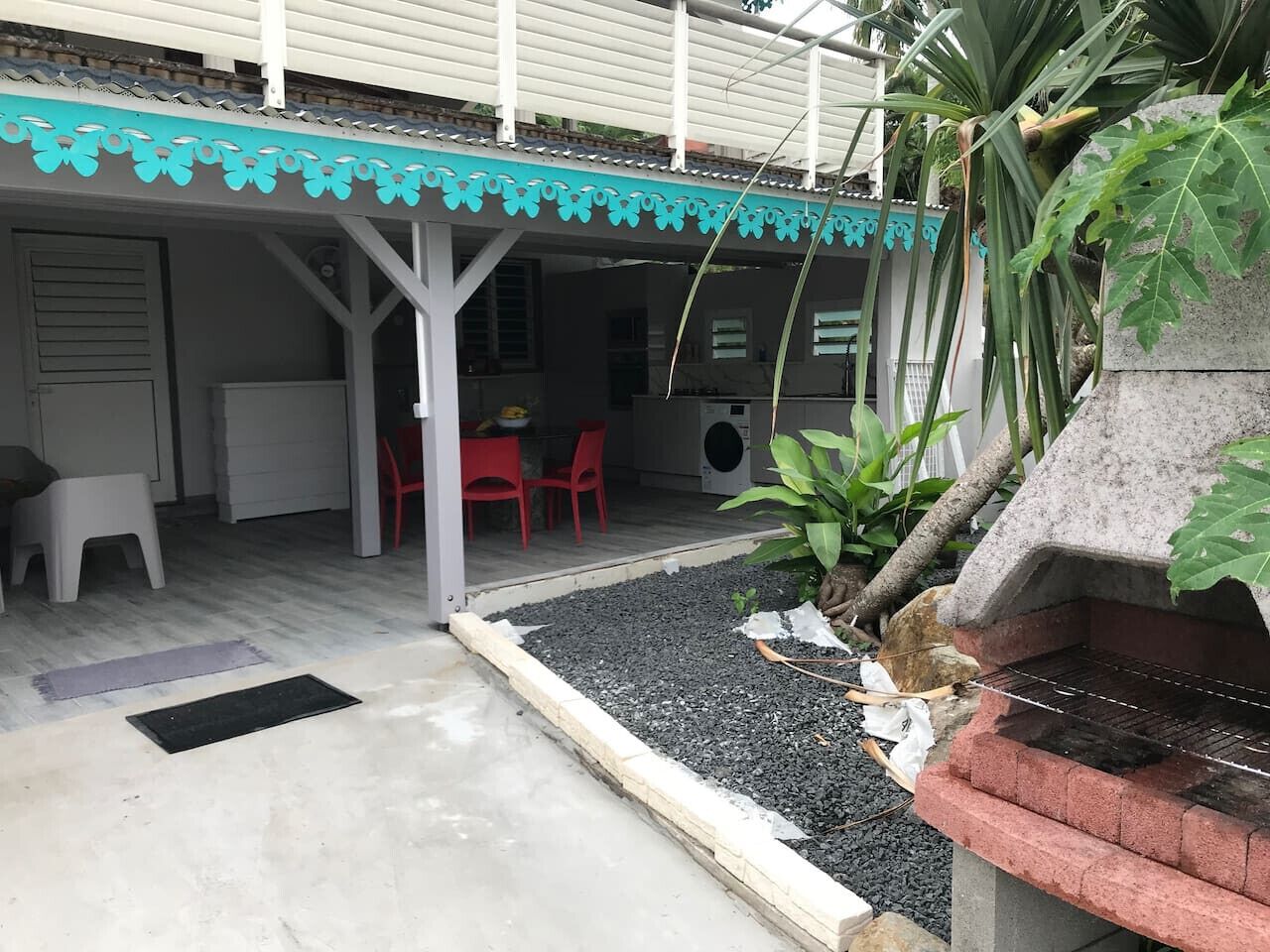 Un patio coperto con barbecue, posti a sedere e un piccolo giardino.