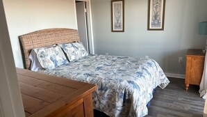 A bedroom with a bed, a wooden nightstand, a dresser, and two framed pictures on the wall. - Fantastic beachfront 2-bedroom condo with AC in pleasant Tybee Island (Tybee Island)