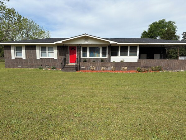 A single-story building with a red door, a covered porch, and a brick facade. - Spacious 3-Bedroom Home with Warm, Welcoming Charm, THE HAPPY HAVEN (Augusta)