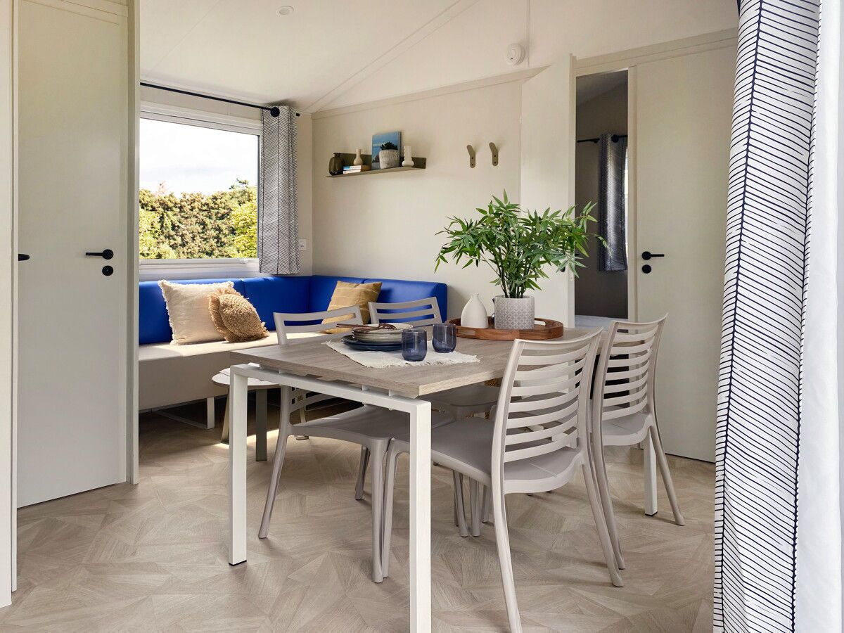 A modern living room with a dining table, white chairs, a blue sofa, and a potted plant.