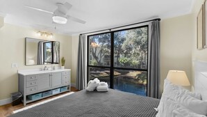 A bedroom with a bed, a large window, a ceiling fan, a vanity with a mirror, and a view of a swimming pool. - Seascape Spacious 3 bedroom w/2 Pool walk to Beach, Celebration Park & Coligny! (Hilton Head Island)