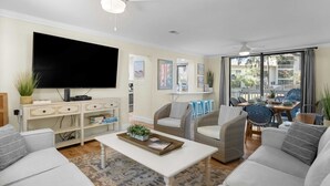 A modern living room with a flat-screen TV, comfortable seating, a coffee table with a plant, and a balcony with outdoor furniture. - Seascape Spacious 3 bedroom w/2 Pool walk to Beach, Celebration Park & Coligny! (Hilton Head Island)