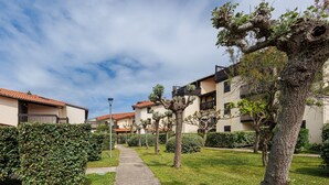 Un sentiero conduce a una fila di edifici con balconi, circondati da siepi e alberi curati.