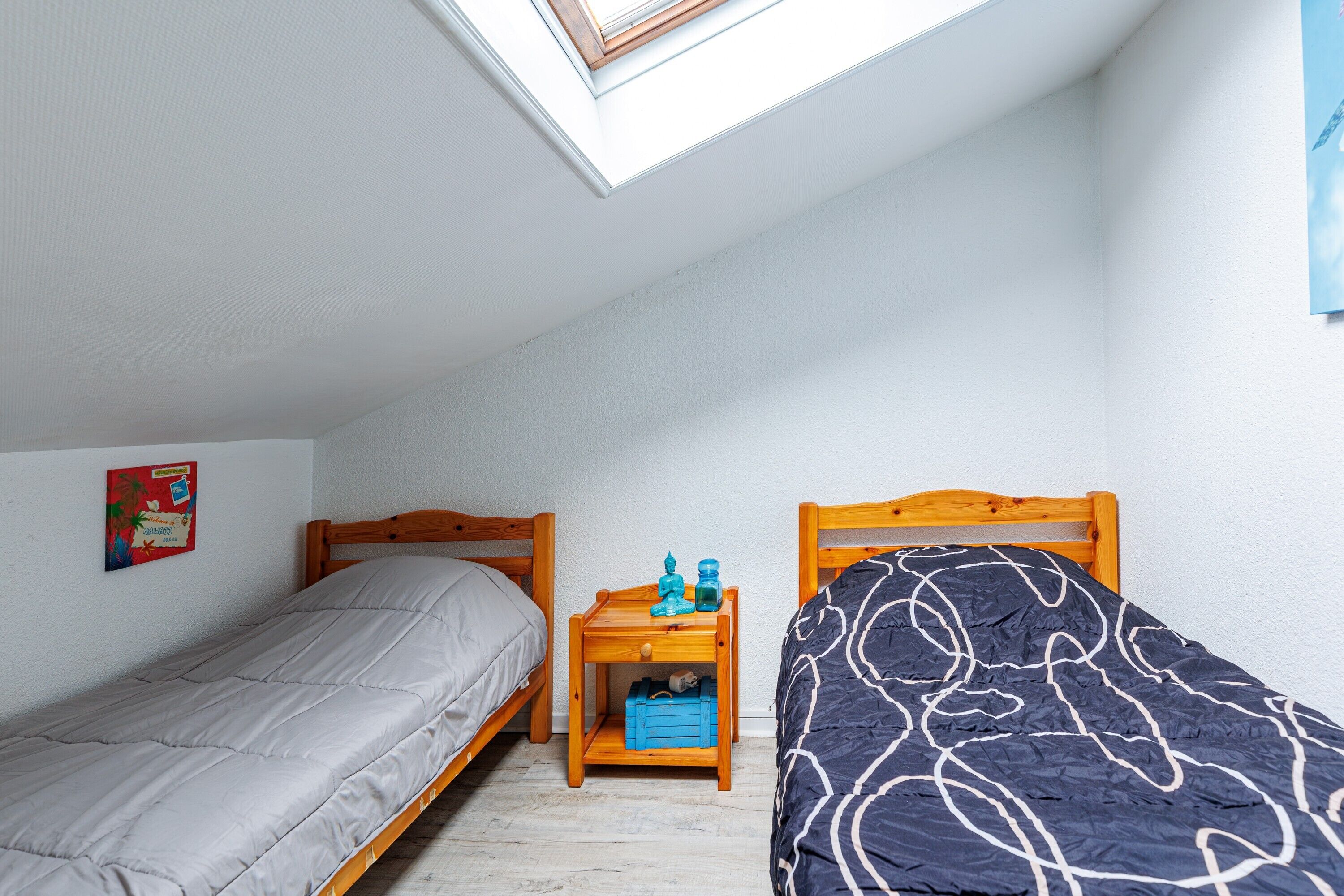 Une chambre de dortoir avec deux lits, une table de chevet en bois et un puits de lumière.