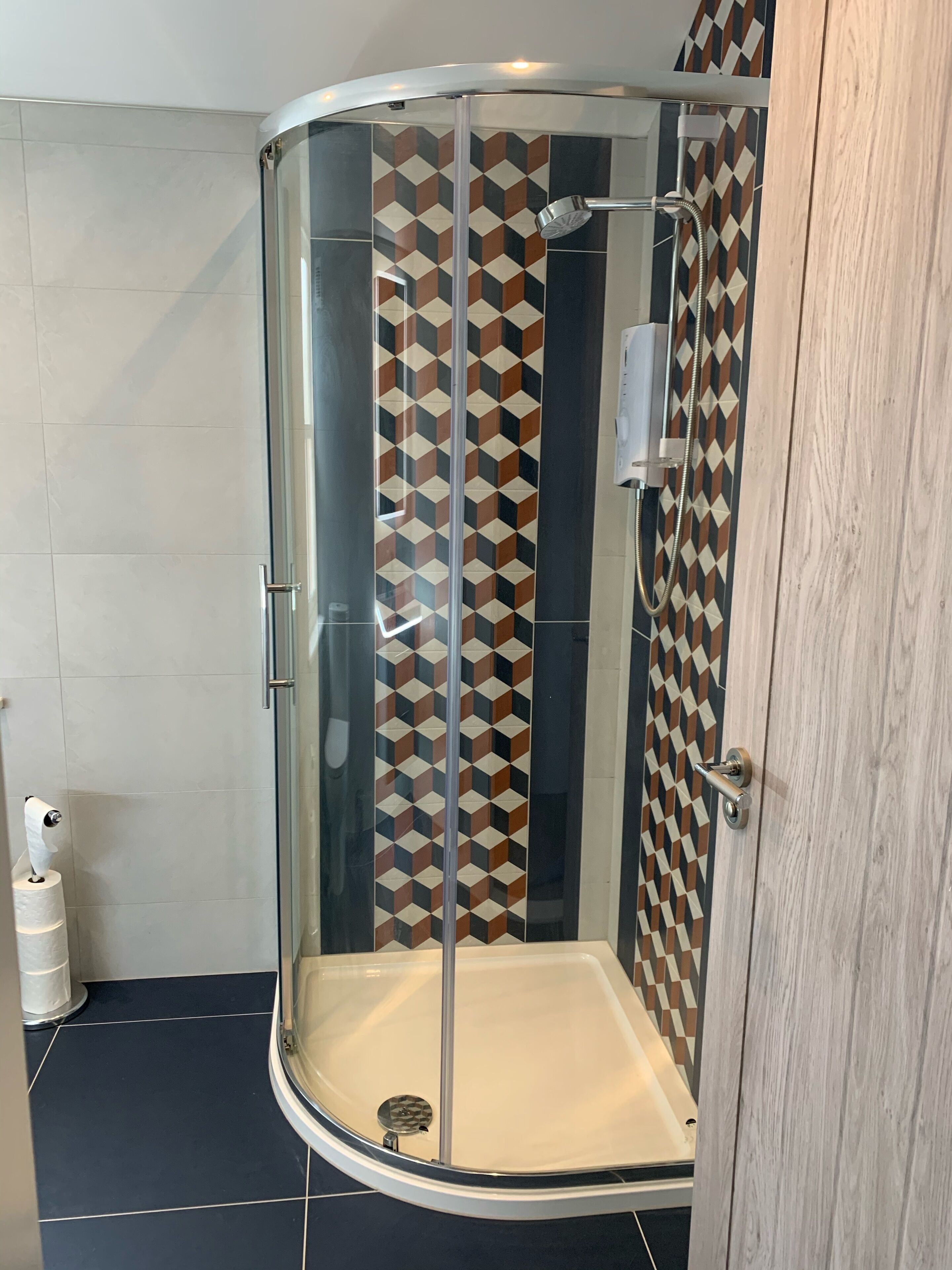 Een douche met glazen wanden, een achterwand van geometrische tegels en een houten deur.