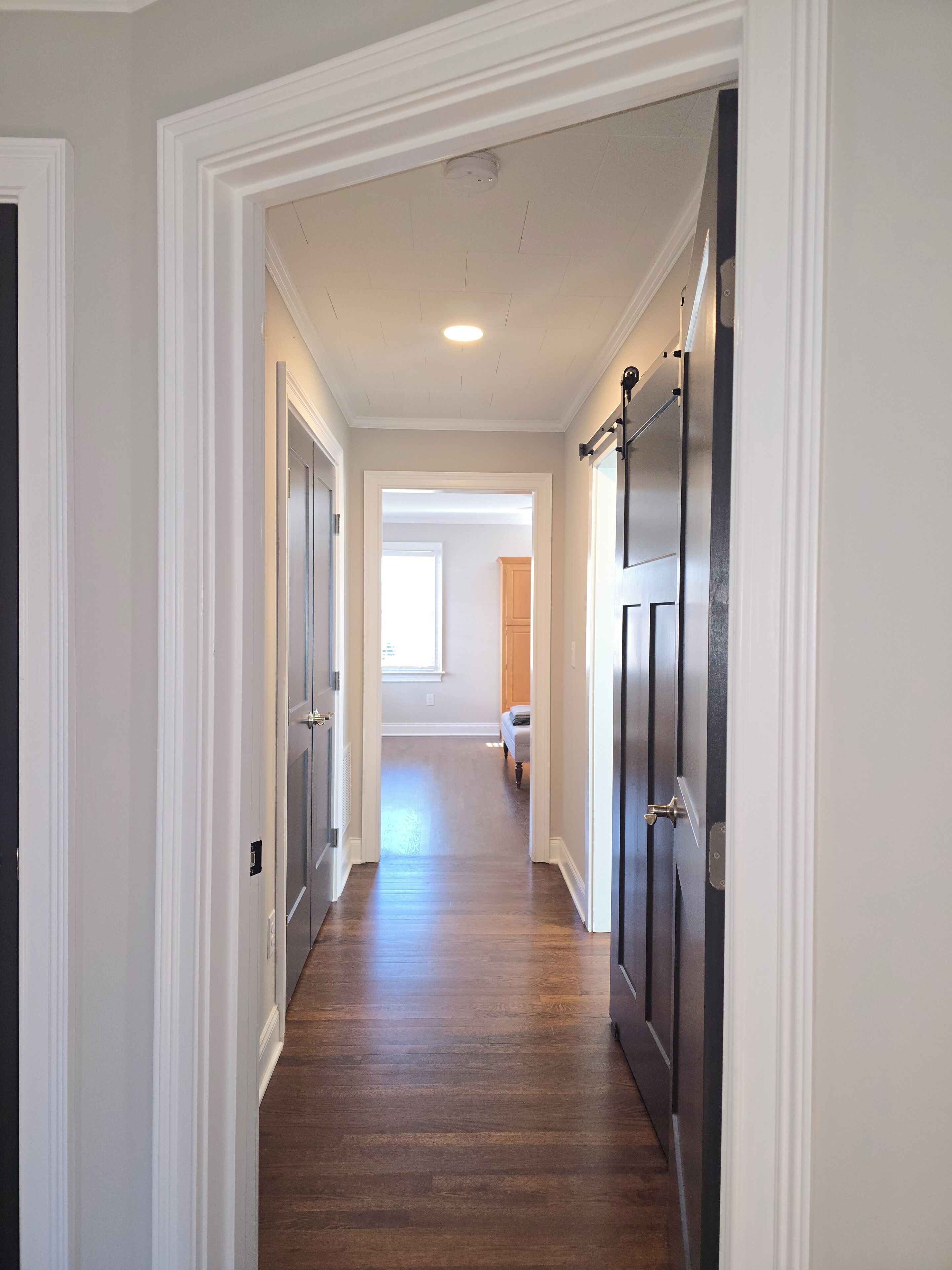 A hallway with wooden flooring, white walls, and dark doors.