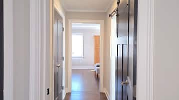 A hallway with wooden flooring, white walls, and dark doors.