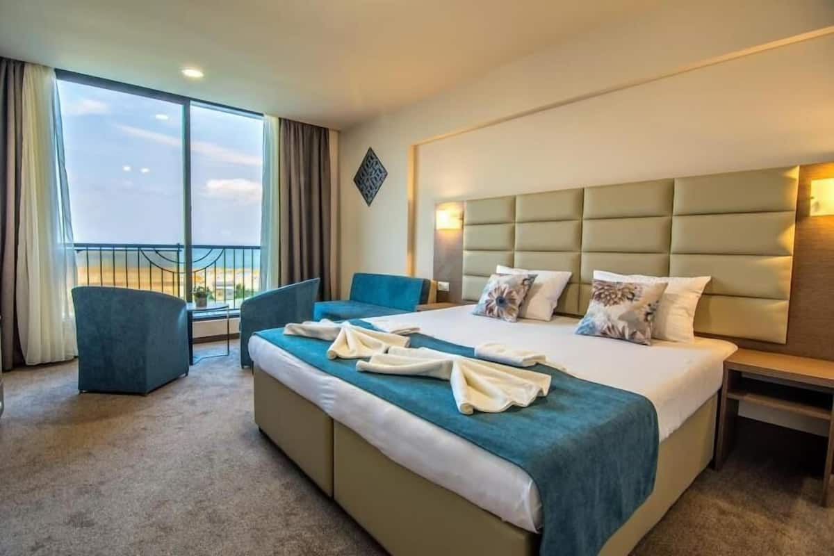 A hotel room with a large bed, a sofa, a chair, and a balcony with a railing.