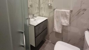 A modern bathroom with a glass shower enclosure, a white sink, a dark vanity, and a toilet. - Independent Room with Private Access in Fairgrounds (Bologna)