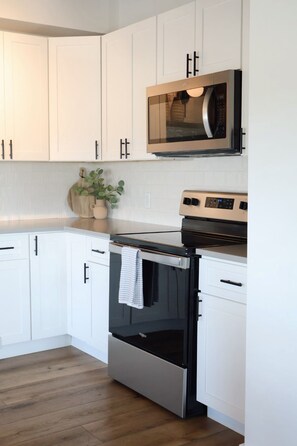 A kitchen with white cabinets, a stainless steel oven, a microwave, and a wooden countertop.