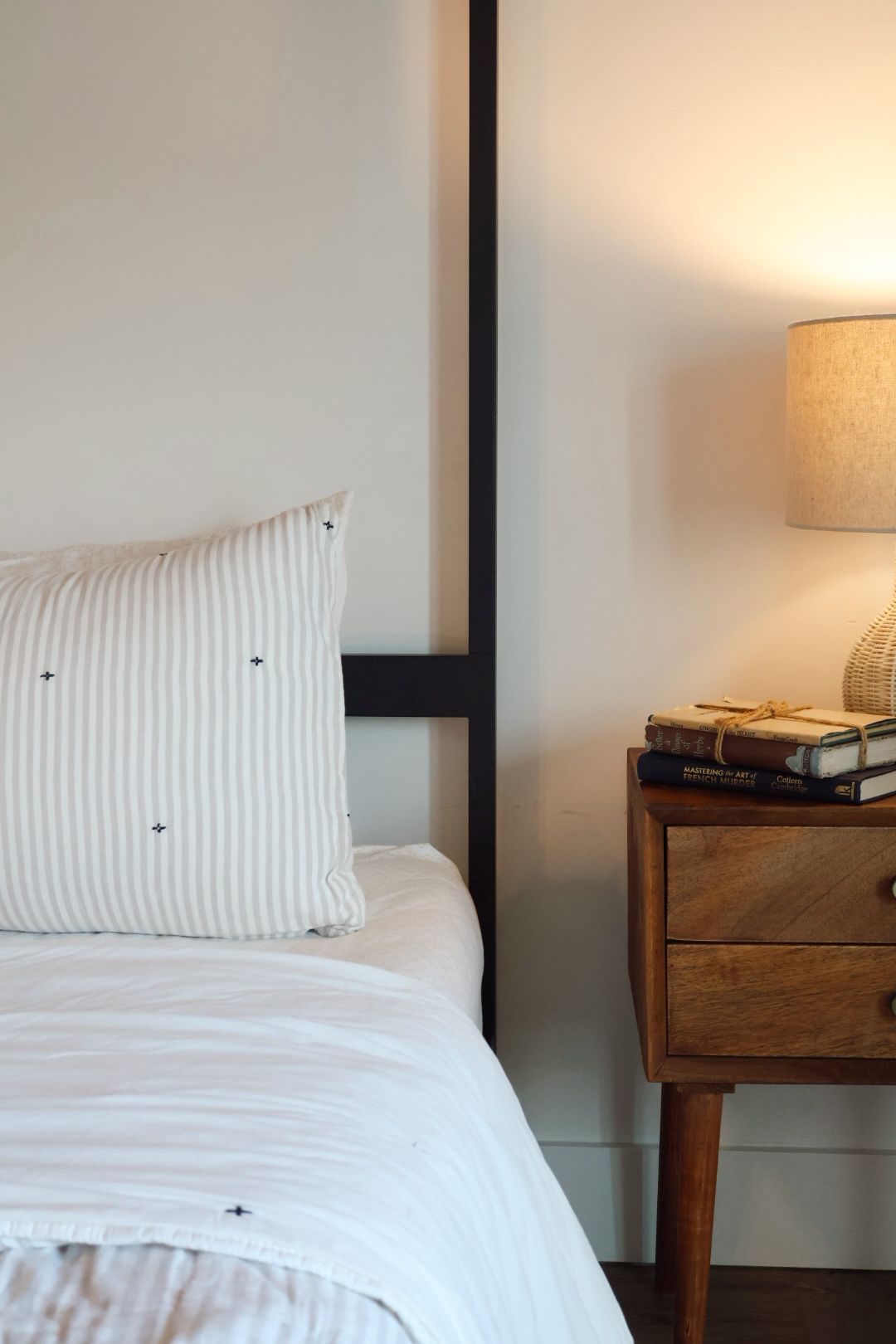 A bed with a striped pillow, a bedside table with a lamp, and a stack of books.