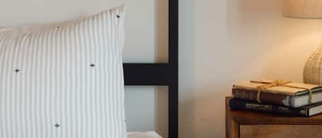 A bed with a striped pillow, a bedside table with a lamp, and a stack of books.