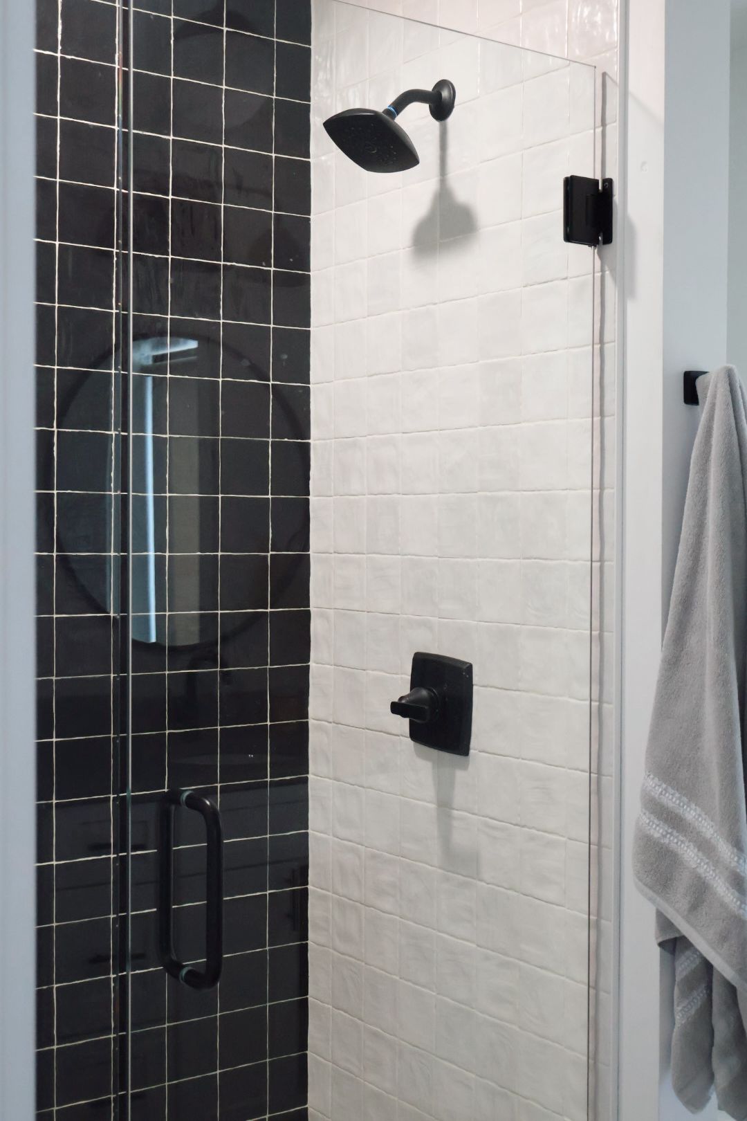 Een douchegedeelte met een zwarte handdouche, een bedieningspaneel aan de muur en een handdoekhouder.