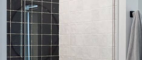 Een douchegedeelte met een zwarte handdouche, een bedieningspaneel aan de muur en een handdoekhouder.