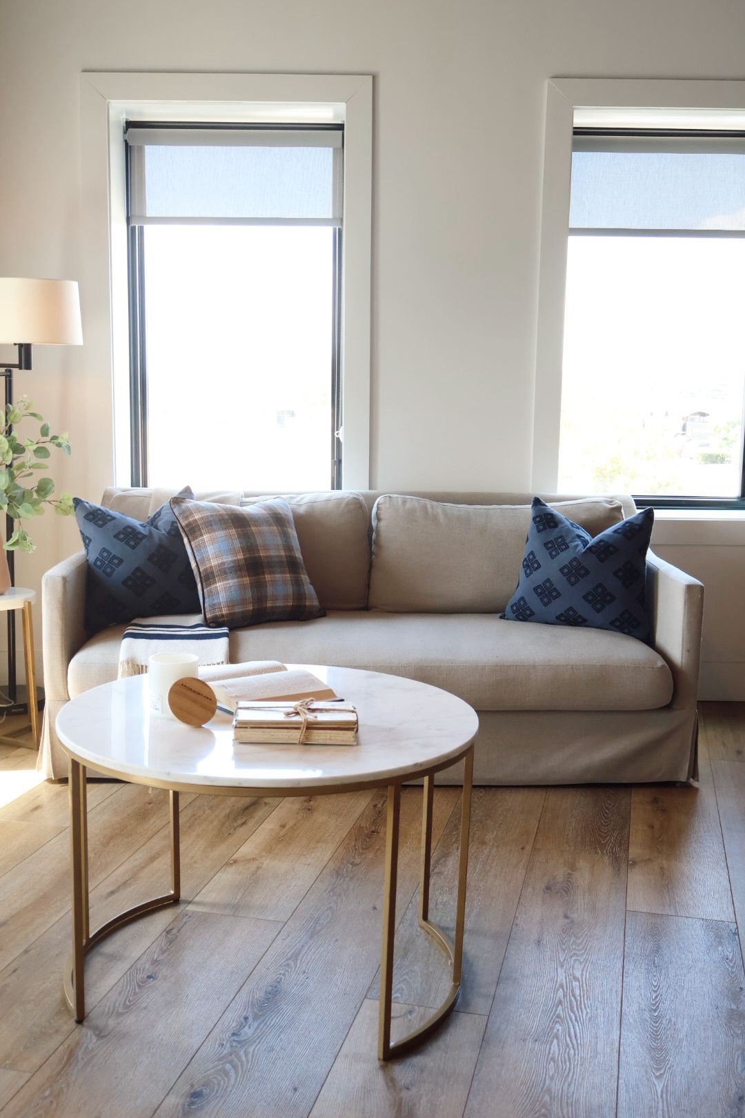 A living room with a sofa, a round coffee table, and two windows.