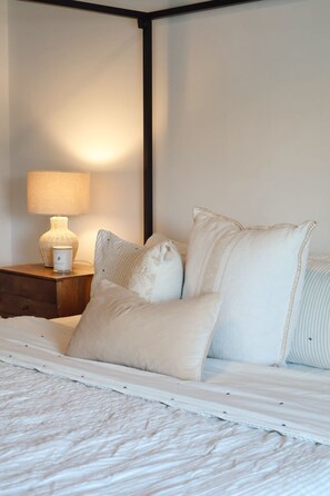 Un letto rifatto con lenzuola e cuscini bianchi, una lampada da comodino e un comodino in legno.
