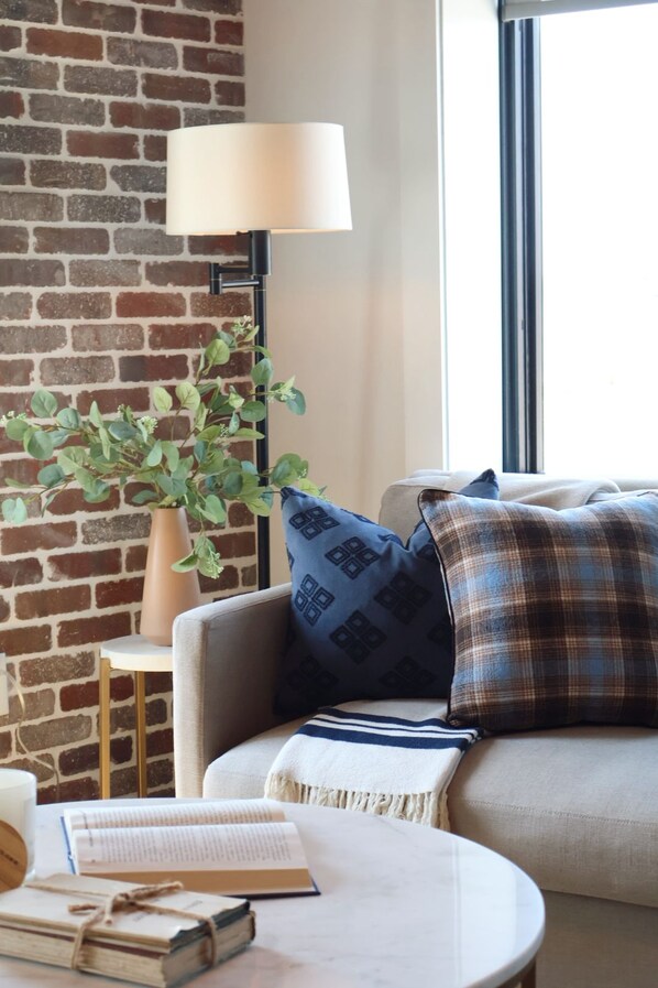 A cozy living area with a brick wall, a sofa, a lamp, a small table, and a plant.