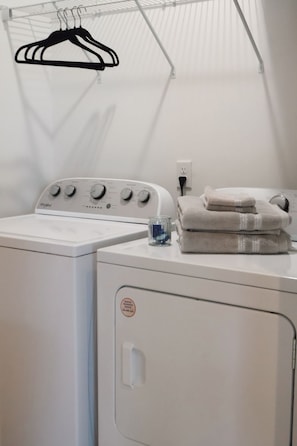 A laundry area with a front-loading washing machine, a dryer, and a hanging rack. - Westside Loft (Cookeville)