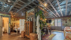 Une pièce rustique avec un plancher en bois, une grande armoire, une table à manger avec des chaises et un lit avec une literie à motifs.