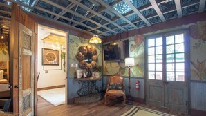 Une pièce dotée d’un plancher en bois, d’un lustre, d’une chaise en bois, d’un mur décoratif orné d’un motif circulaire et d’une fenêtre donnant sur l’extérieur.
