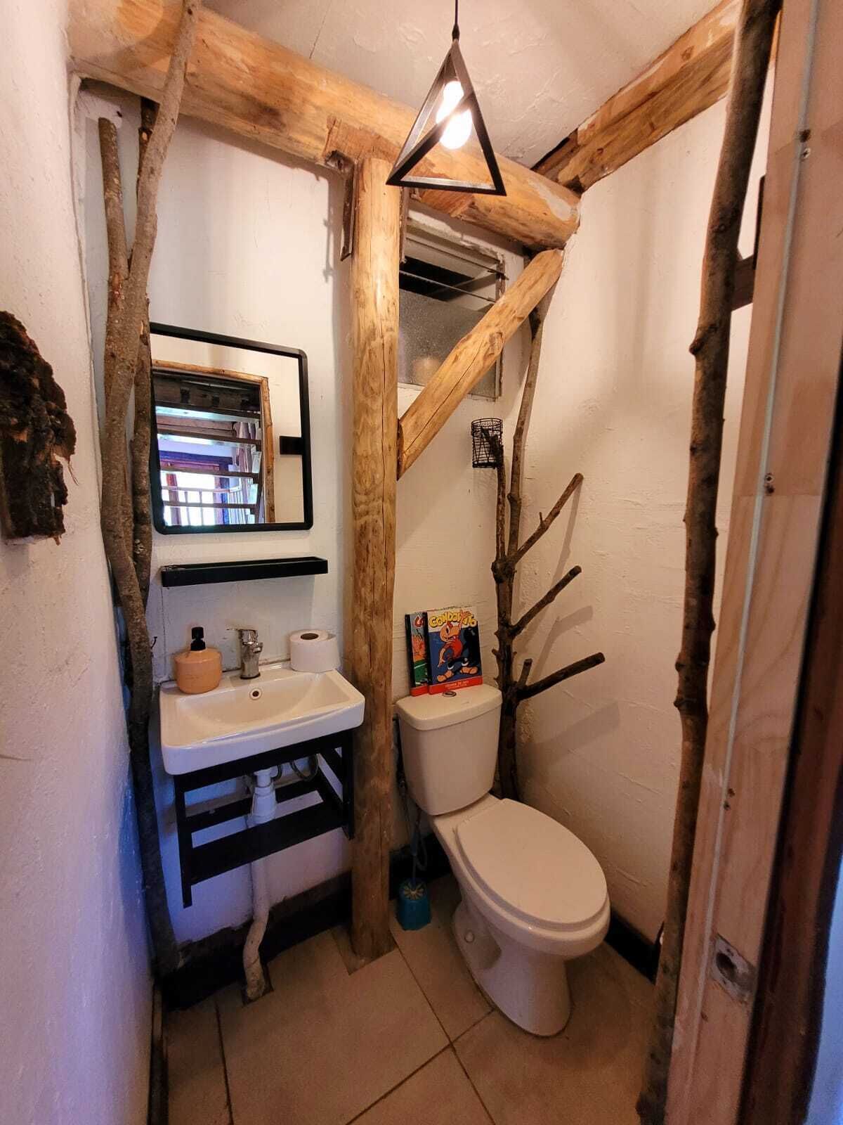 A compact bathroom with a wooden beam structure, a white sink, a toilet, and a hanging light fixture.