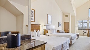A hotel room with two beds, a desk, a chair, a lamp, and a window with blinds.