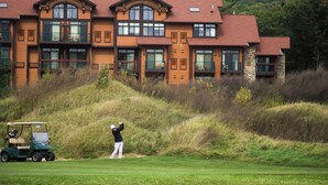 A multi-story building with a red roof and large windows, situated near a golf course.