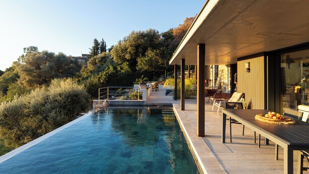 Area piscina moderna all'aperto con un solarium in legno, poltrone a sdraio e un tavolo da pranzo con frutta.