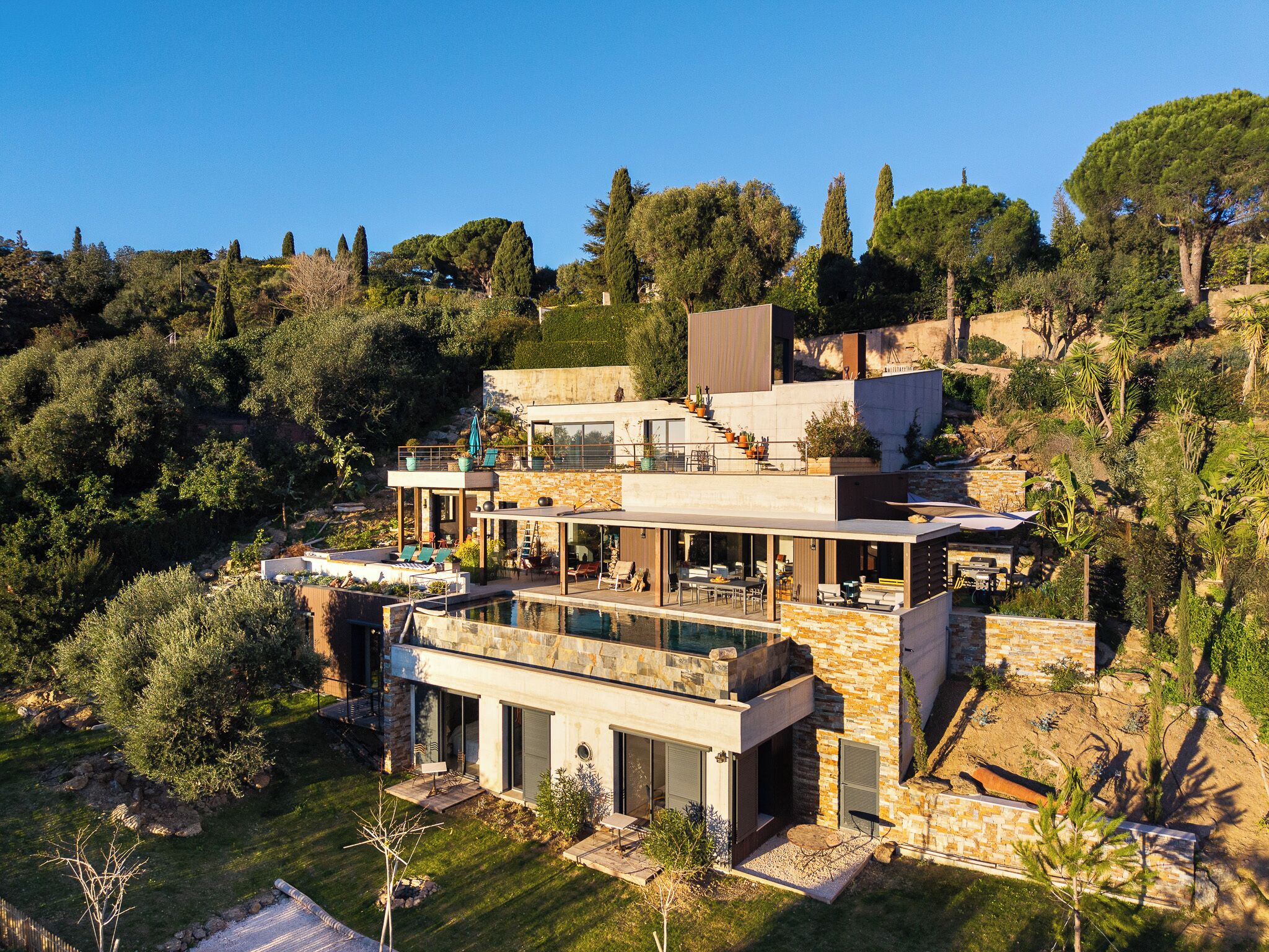 Una casa moderna de dos pisos con piscina en la azotea, rodeada de exuberante vegetación y árboles.