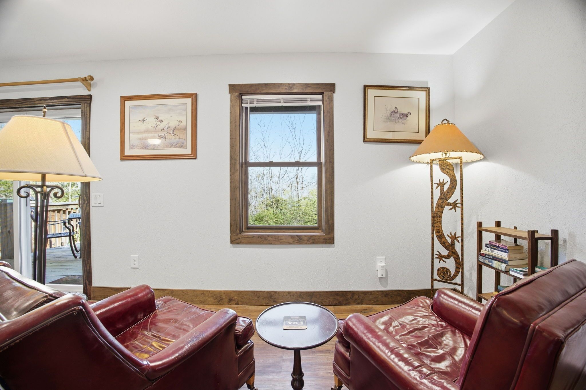 A room with two leather sofas, a small round table, a window with blinds, and two wall-mounted lamps.