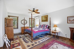 A bedroom with a four-poster bed, a ceiling fan, a wooden dresser, a nightstand, a lamp, and a fireplace. - Secluded Franklin Cabin with Mountain Views (Franklin)