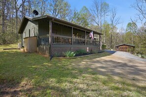 A cabin with a porch, a flag, and a small shed in a wooded area. - Secluded Franklin Cabin with Mountain Views (Franklin)
