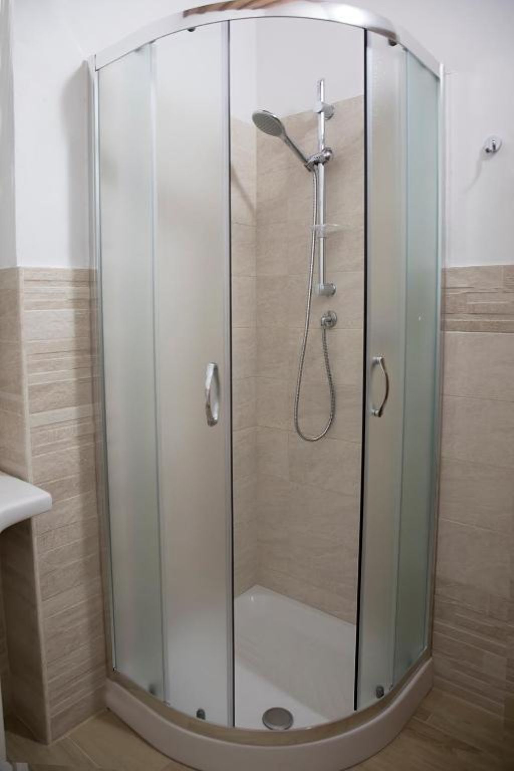 A glass-enclosed shower stall with a handheld showerhead and a wall-mounted faucet.