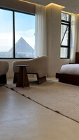 A modern hotel room with a large window offering a view of a pyramid and cityscape. There is a bed, a sofa, and a small table.