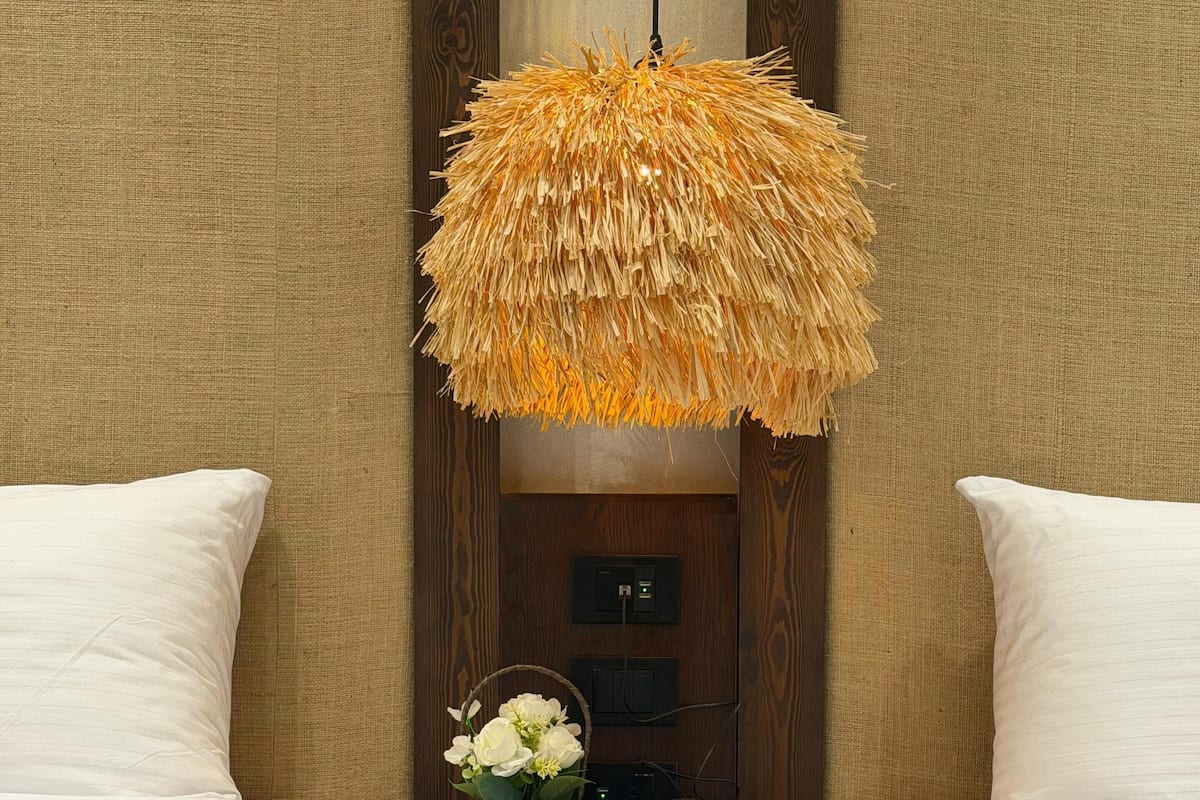 A hotel room with two beds, a nightstand with a telephone and a vase of flowers, and a unique textured hanging light fixture.