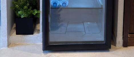 A compact refrigerator with a glass door, containing various beverages and a kettle on top.