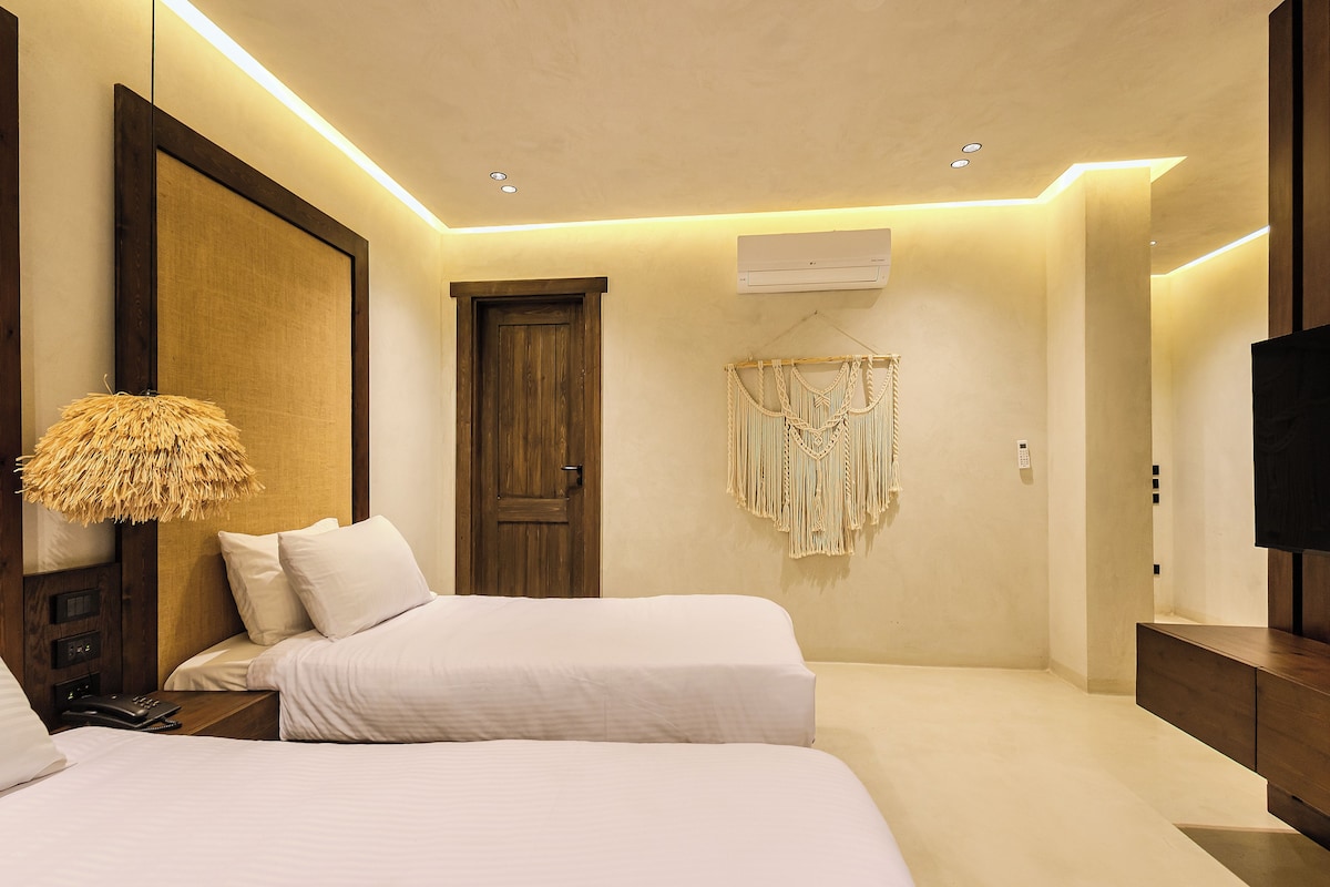 Une chambre d’hôtel avec deux lits, un grand miroir, un climatiseur fixé au mur et un téléviseur posé sur un meuble en bois.