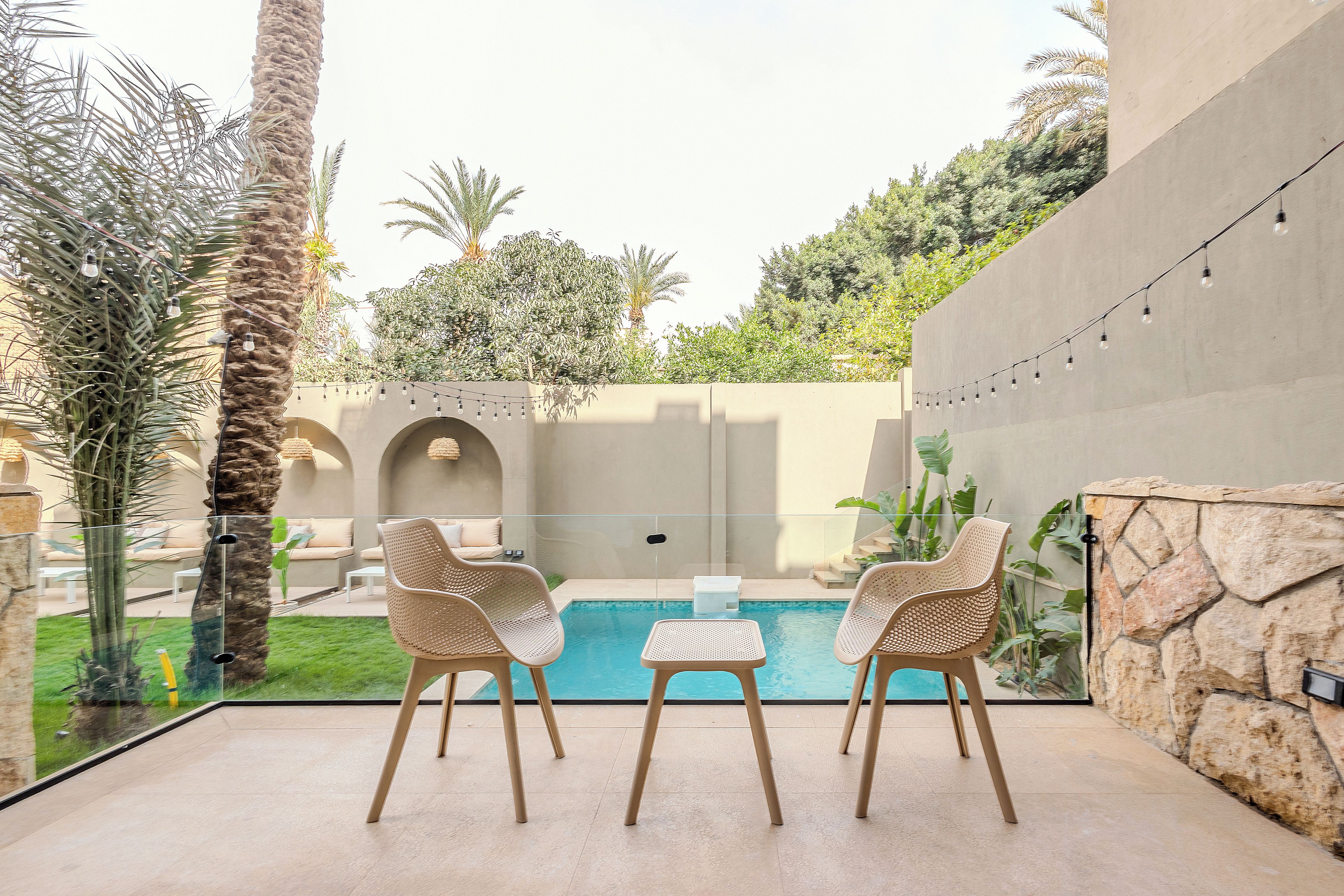 A poolside area with two wicker chairs, a glass table, and a view of a swimming pool.