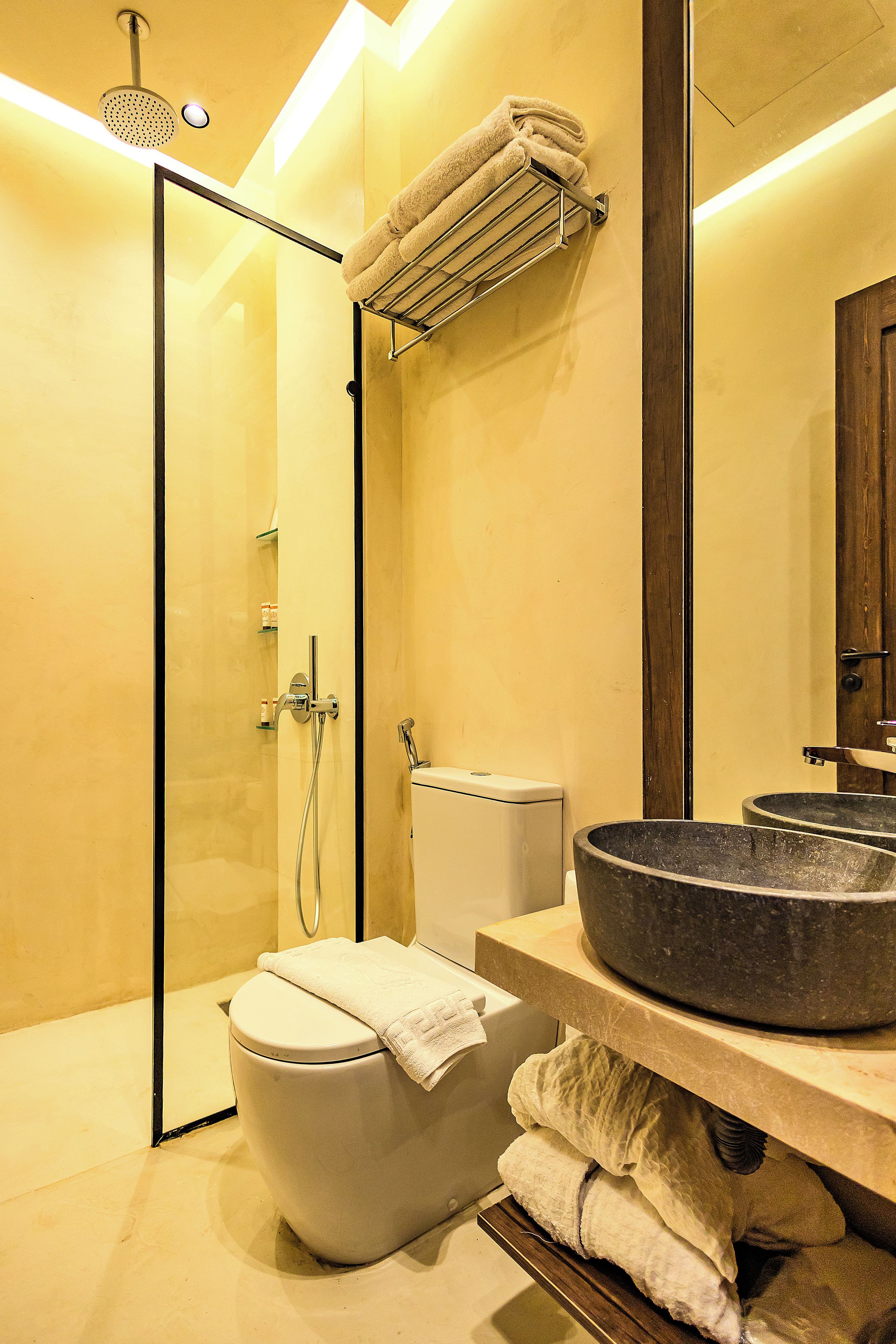 A modern bathroom with a glass shower enclosure, a toilet, and a large stone sink.