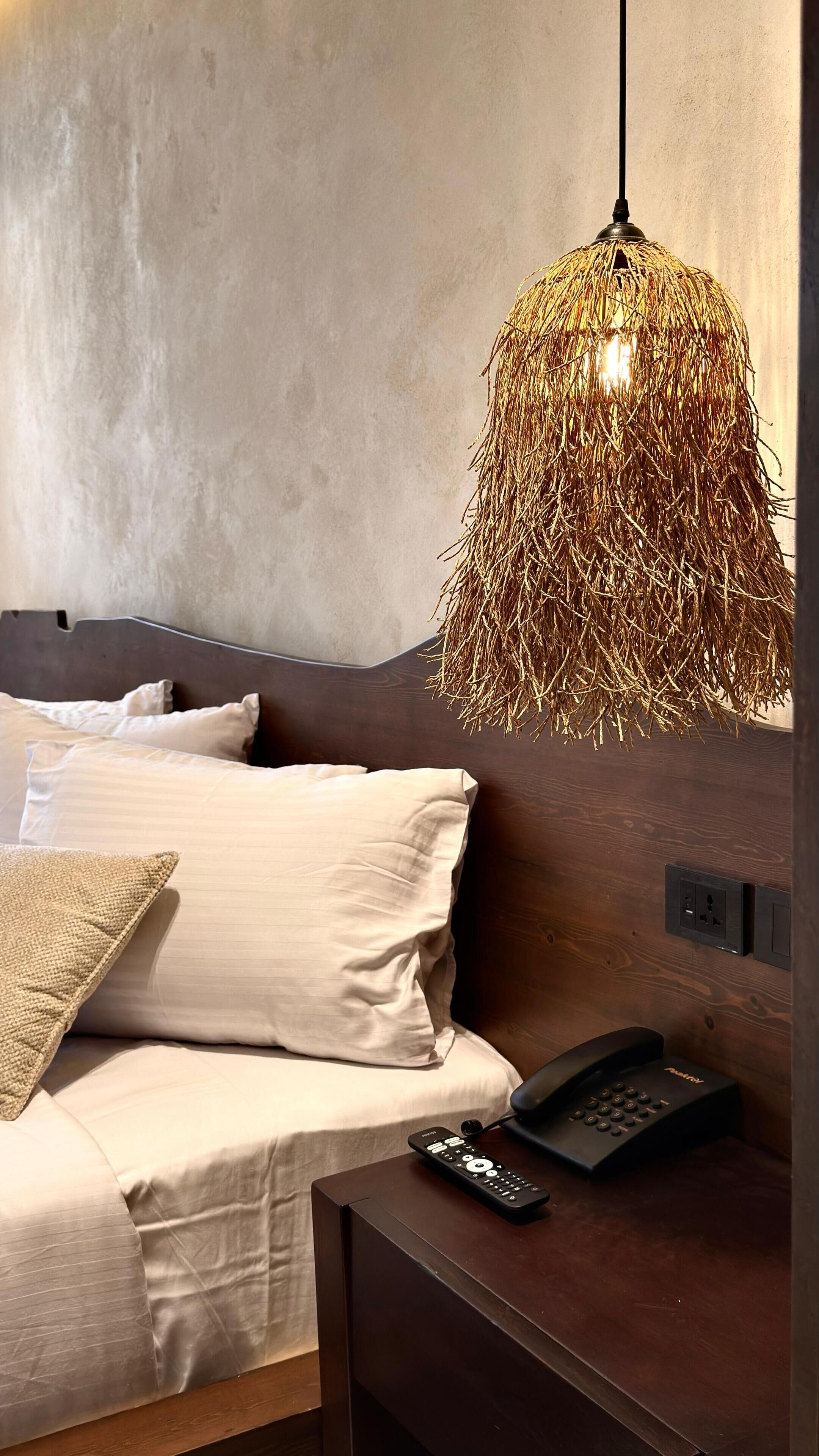 Una camera da letto moderna con un letto, un comodino, un telecomando e un'originale lampada a sospensione in fibra.