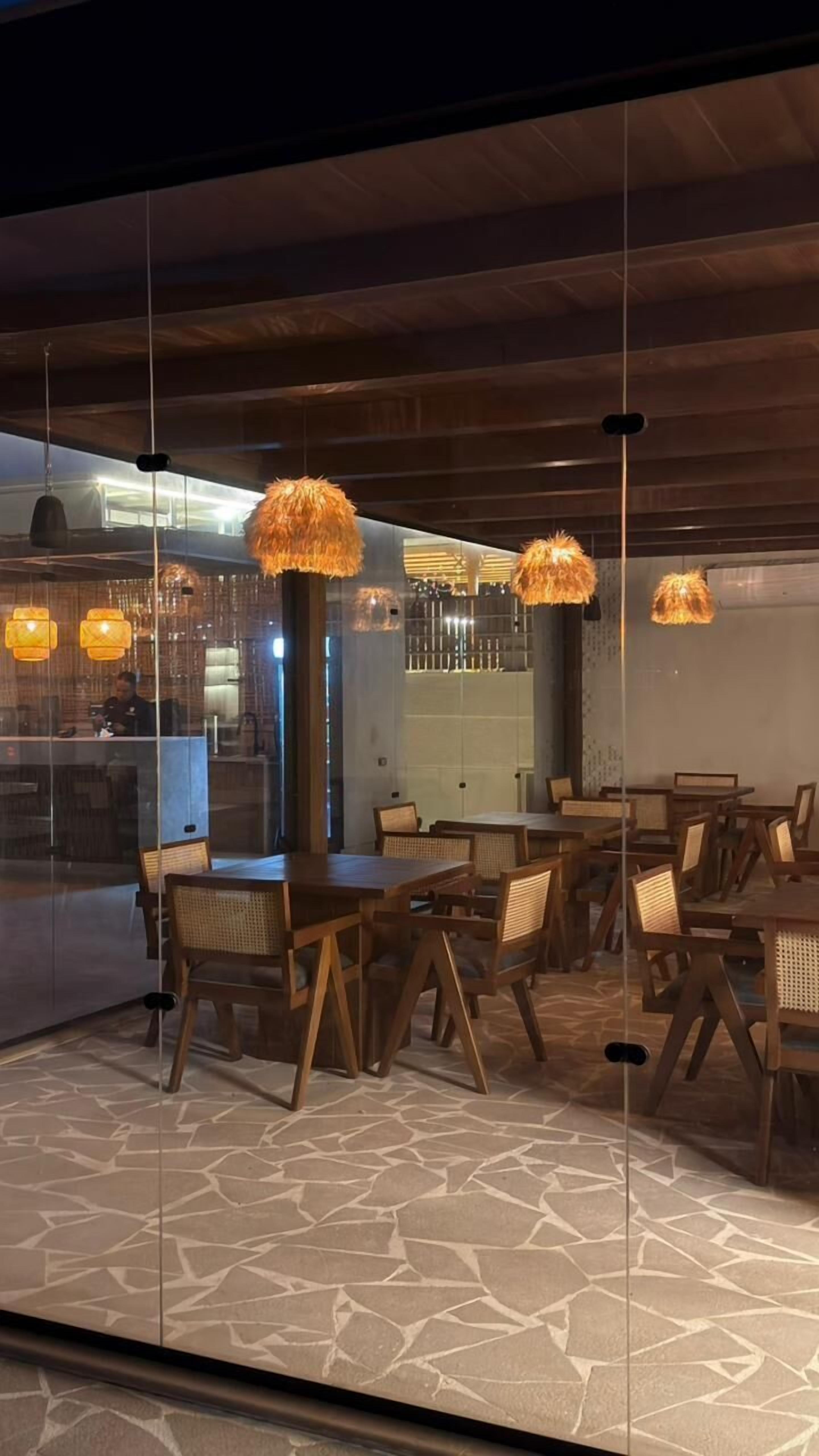 A restaurant with wooden tables and chairs, hanging lamps, and a stone floor.